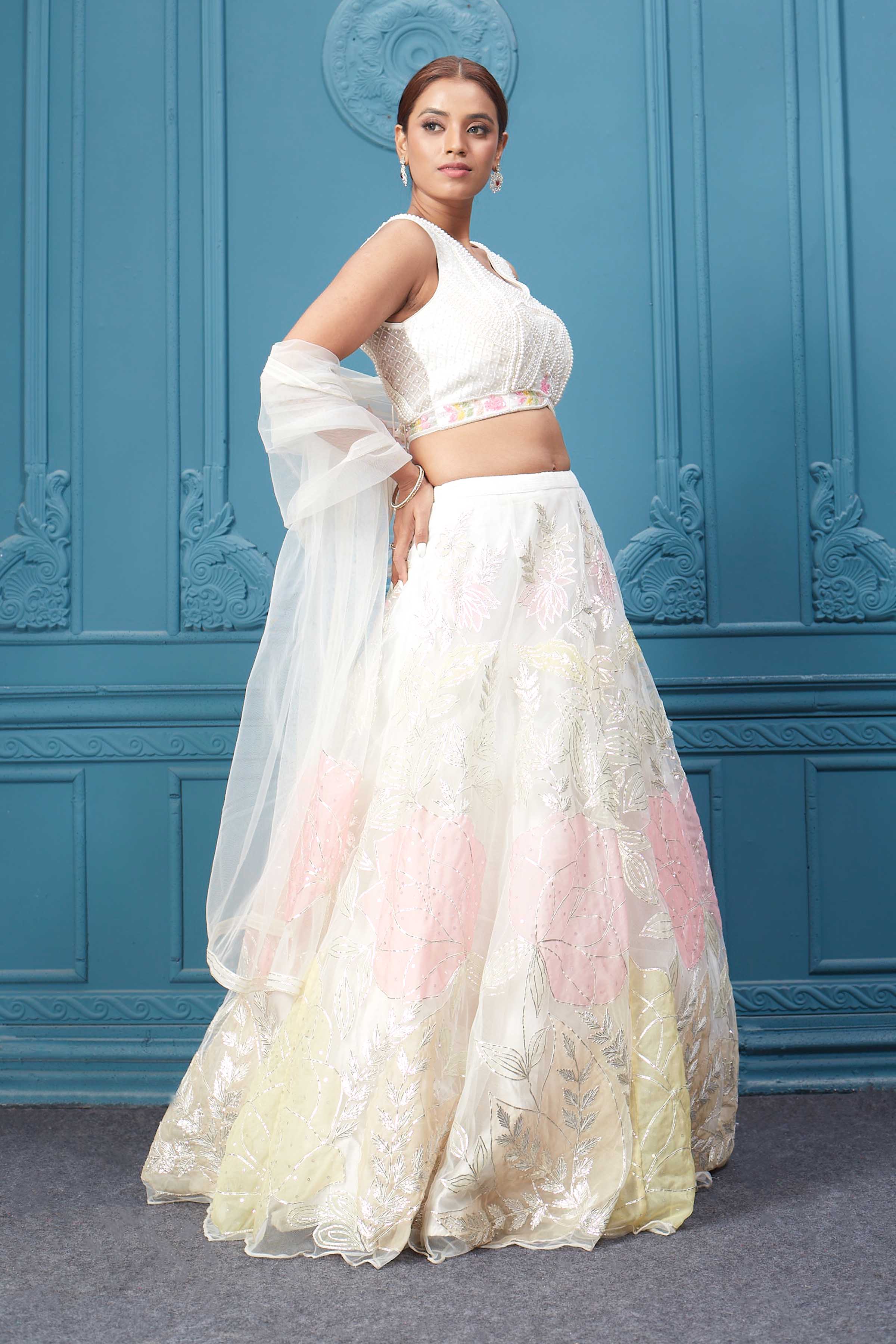 Shop an off-white floral lehenga with silver embroidery and a sleeveless blouse. Dazzle on weddings and special occasions with exquisite Indian designer dresses, sharara suits, Anarkali suits, bridal lehengas, and sharara suits from Pure Elegance Indian clothing store in the USA. Shop online from Pure Elegance.