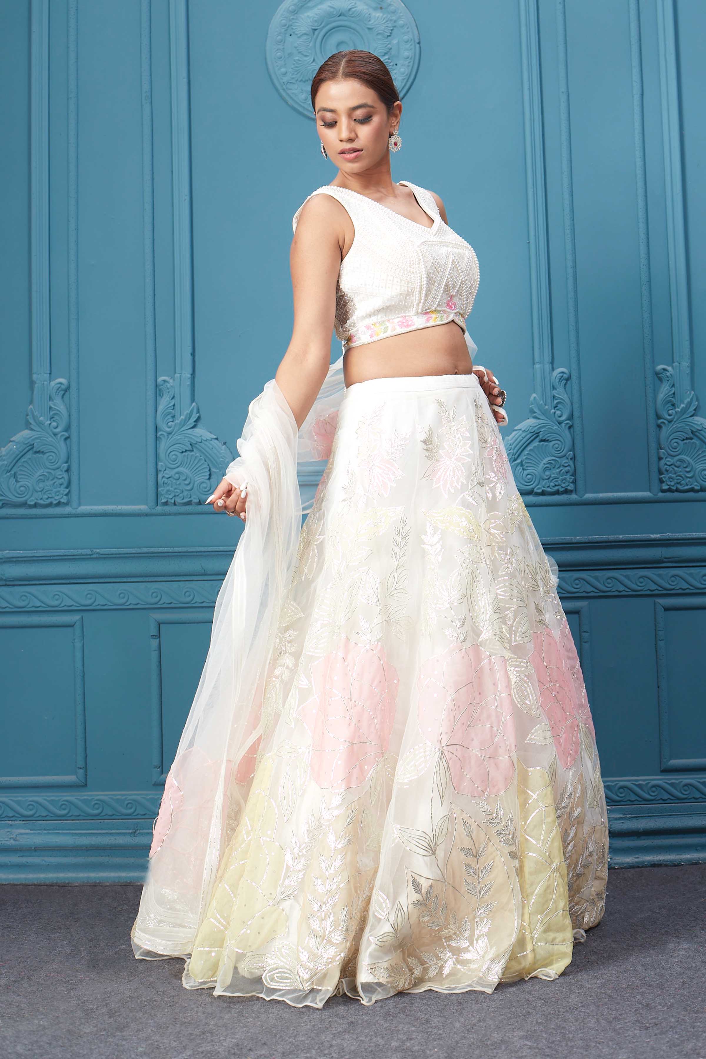 Shop an off-white floral lehenga with silver embroidery and a sleeveless blouse. Dazzle on weddings and special occasions with exquisite Indian designer dresses, sharara suits, Anarkali suits, bridal lehengas, and sharara suits from Pure Elegance Indian clothing store in the USA. Shop online from Pure Elegance.