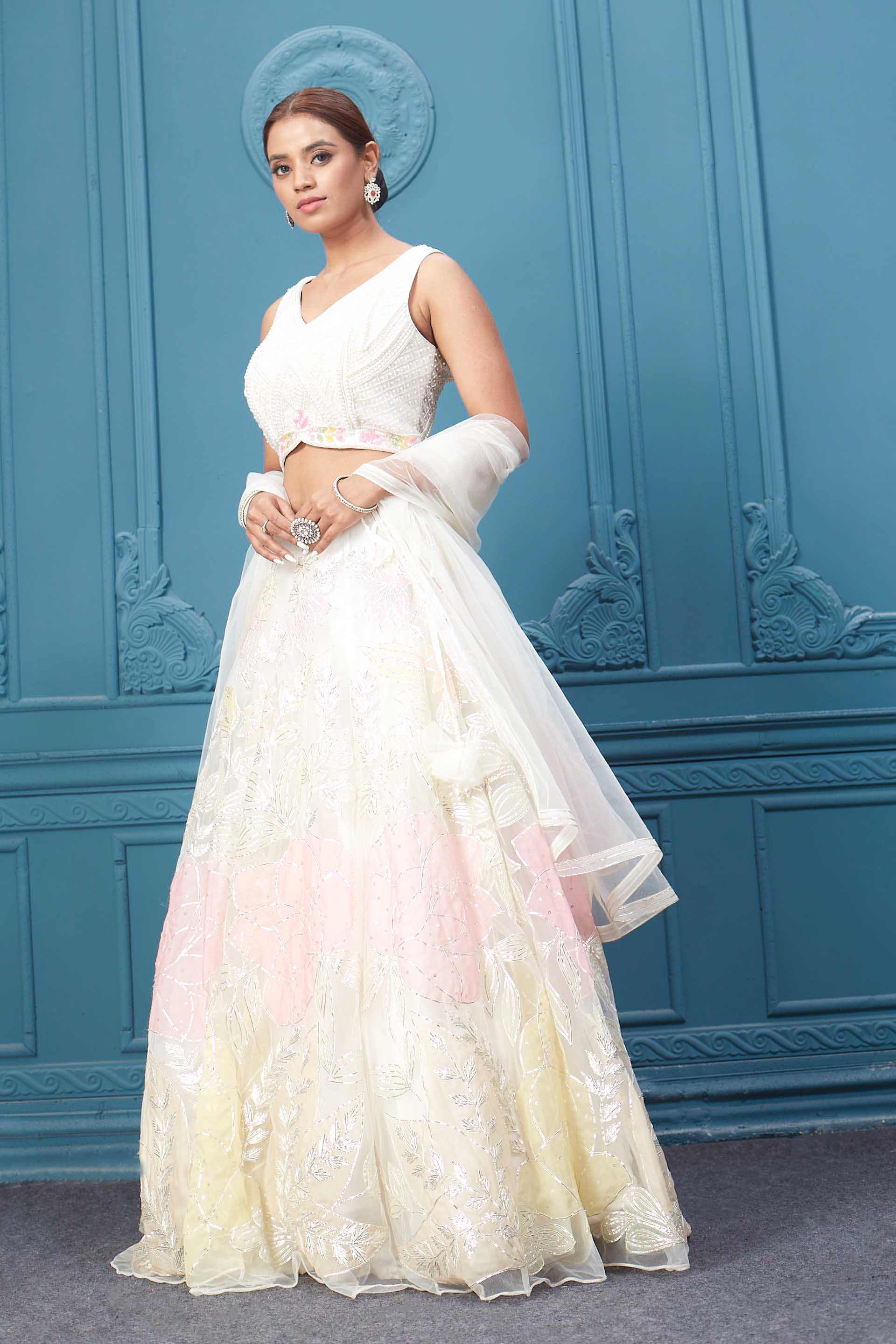 Shop an off-white floral lehenga with silver embroidery and a sleeveless blouse. Dazzle on weddings and special occasions with exquisite Indian designer dresses, sharara suits, Anarkali suits, bridal lehengas, and sharara suits from Pure Elegance Indian clothing store in the USA. Shop online from Pure Elegance.