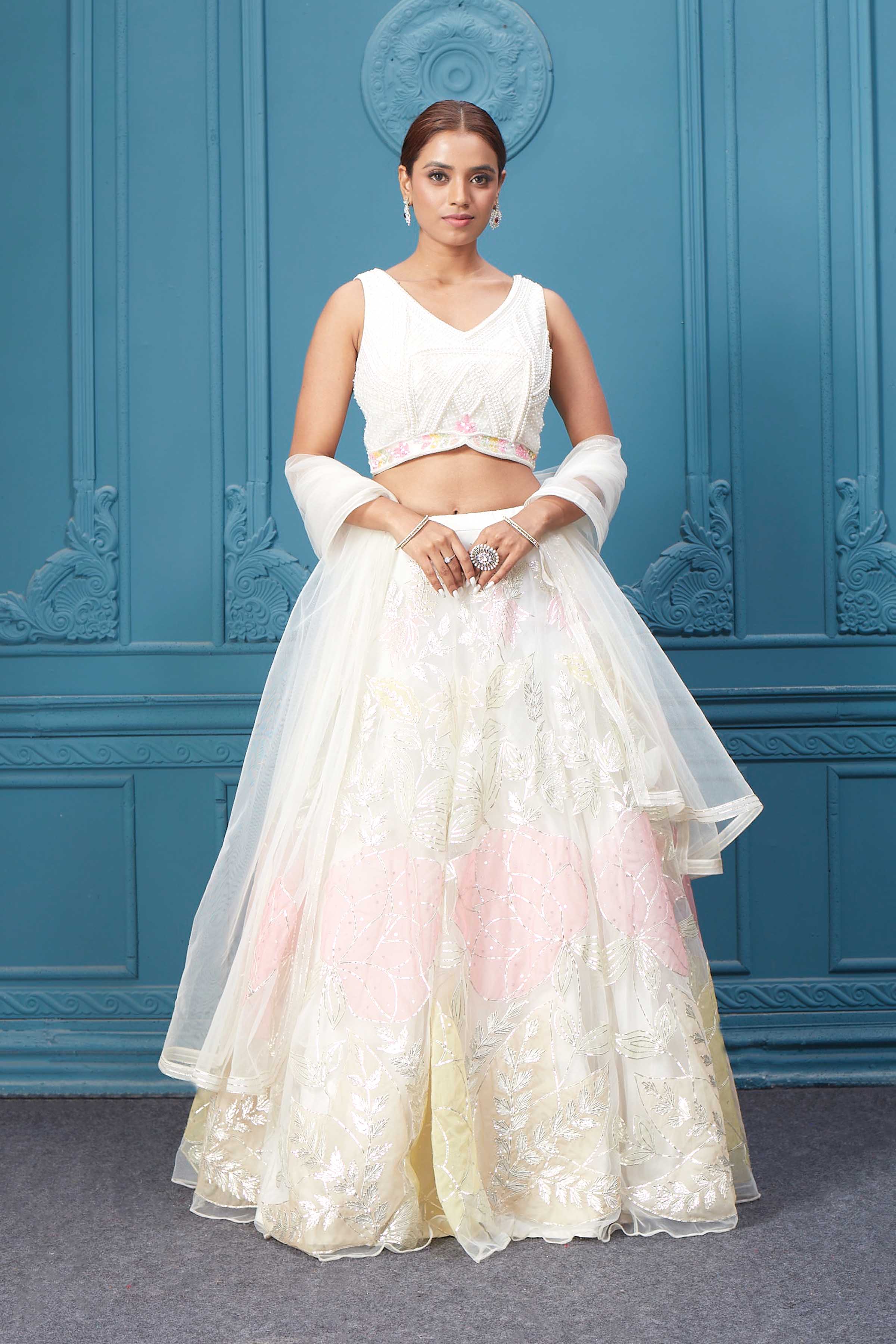 Shop an off-white floral lehenga with silver embroidery and a sleeveless blouse. Dazzle on weddings and special occasions with exquisite Indian designer dresses, sharara suits, Anarkali suits, bridal lehengas, and sharara suits from Pure Elegance Indian clothing store in the USA. Shop online from Pure Elegance.